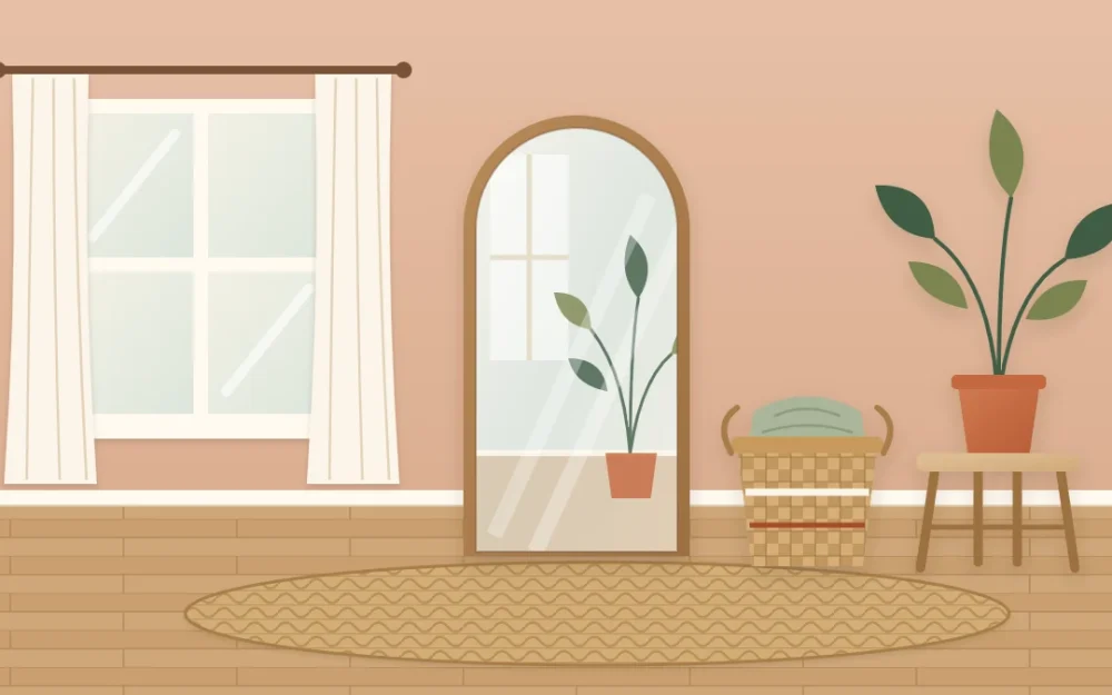 A tall arched floor mirror in a slim wooden frame leaning on a clay-colored wall beside a window, with a basket and stool