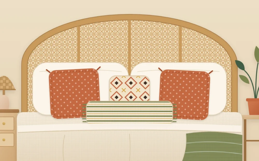 The head of a bed with two cream sleeping pillows, two terracotta squares, a patterned square and a long fringed lumbar pillow